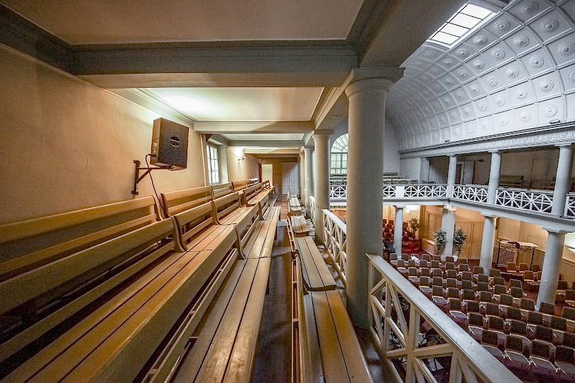 Nef latérale Est avant travaux. Vue vers la porte d’accès de la cage d’escaliers. Le dispositif de gradins et de bancs rendait difficile la perception de l’espace en contrebas dans la nef et la circulation était problématique.
